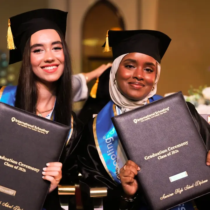 Two International Schooling graduates holding their diplomas at the Class of 2026 ceremony