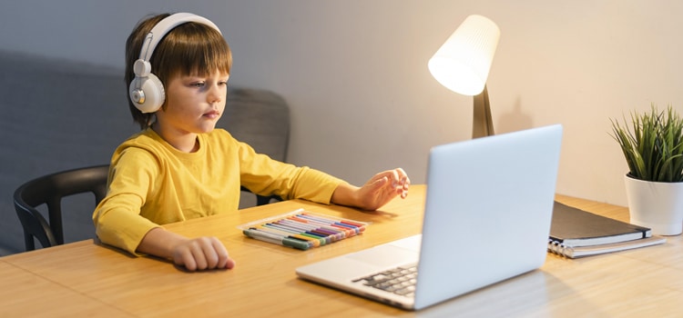 An elementary enrolled student sitting in front of laptop and doing homework
